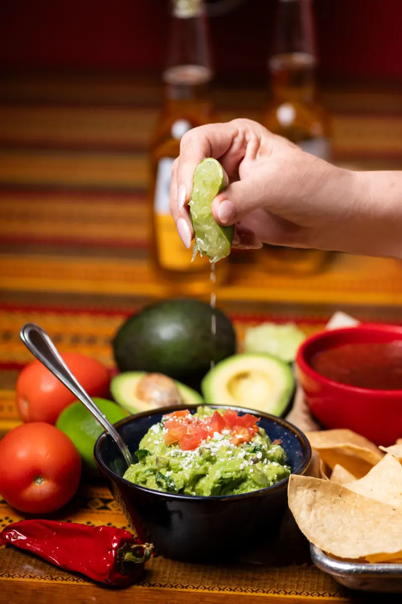 Fresh lime squeezed over guacamole with tortilla chips, avocados and tomatoes