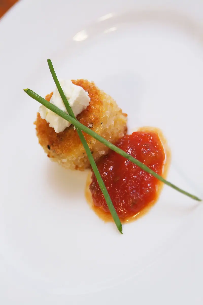 Plated appetizer: crispy risotto cake with goat cheese, tomato coulis and chives