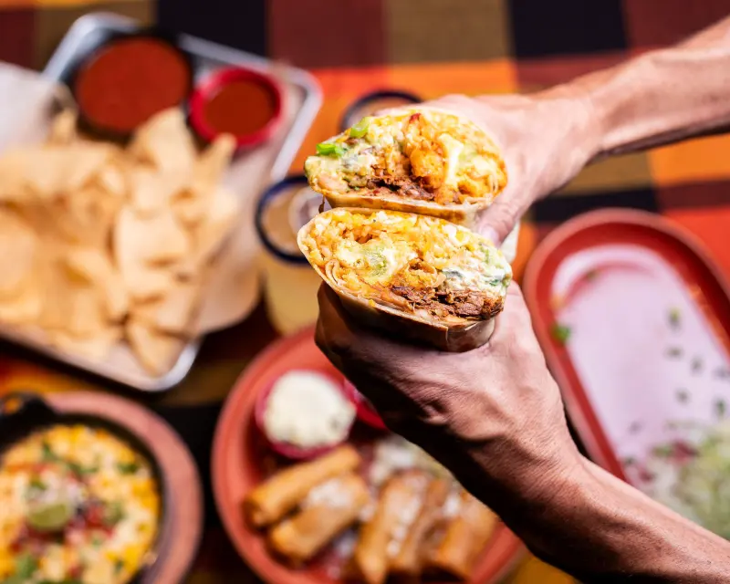 Burrito cut in half over a table of chips, salsa and Mexican restaurant dishes