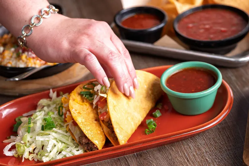 Hand reaching for crispy beef tacos with salsa and shredded lettuce