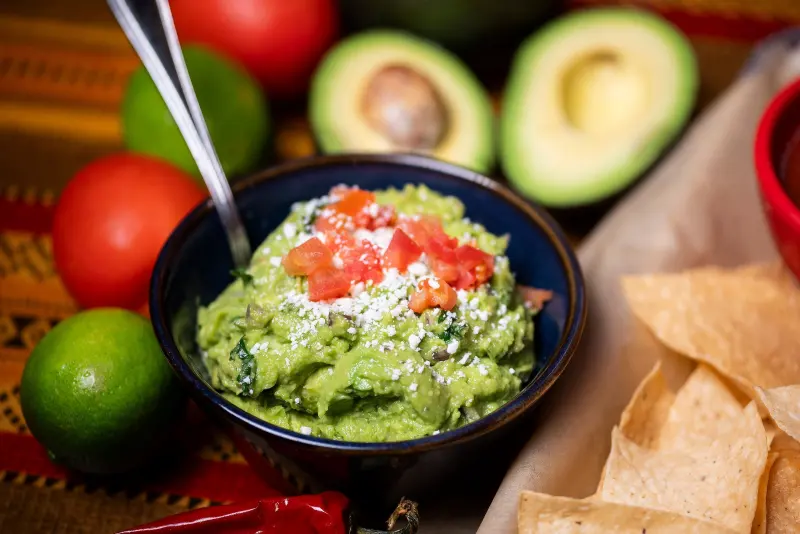 Guacamole with diced tomato, tortilla chips, limes and avocados