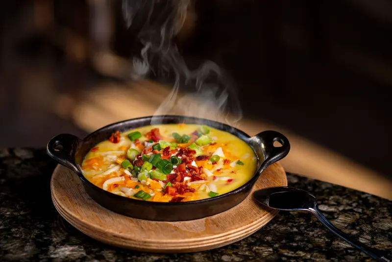 Steaming queso fundido skillet topped with bacon and pico de gallo